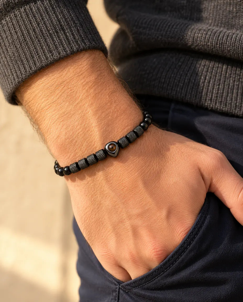 Uomo che indossa il bracciale di perline nero con cuore e foto dentro, pollice infilato in tasca