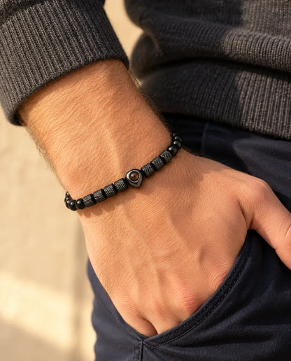 Uomo che indossa il bracciale di perline nero con cuore e foto dentro, pollice infilato in tasca