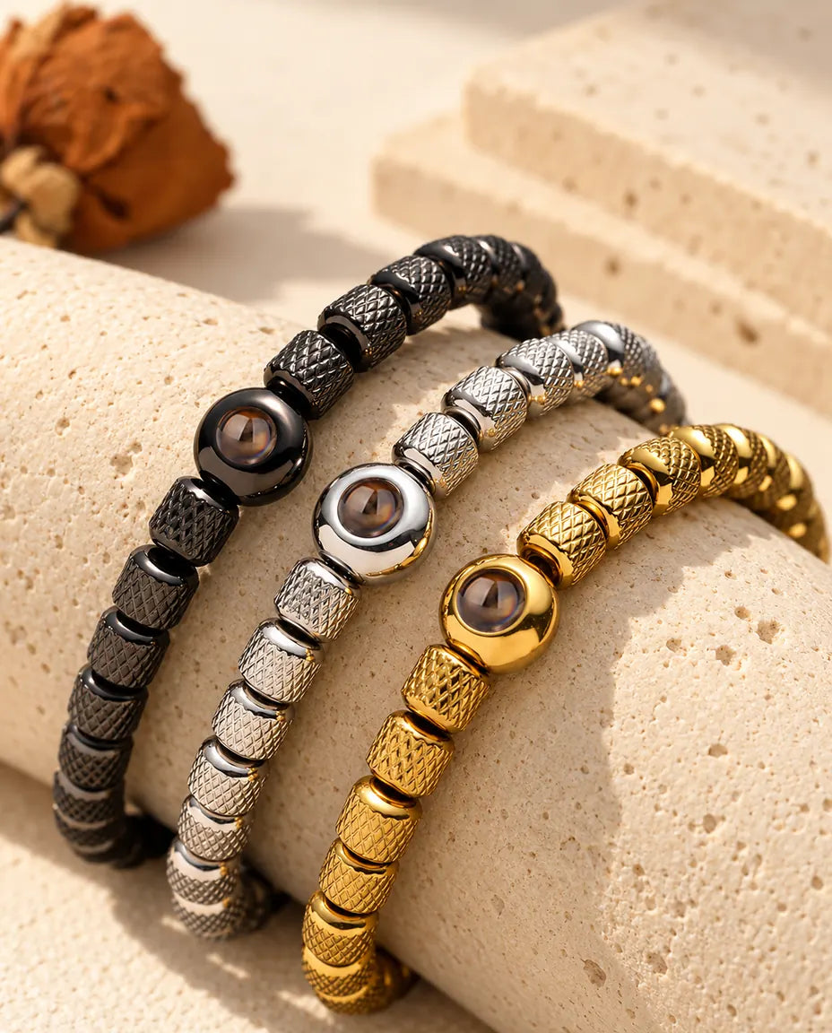Tre bracciali di perline, nero, argentato e dorato, adagiati su un blocco di travertino