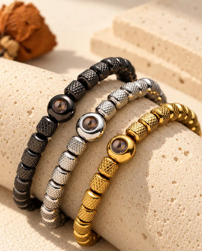 Tre bracciali di perline, nero, argentato e dorato, adagiati su un blocco di travertino