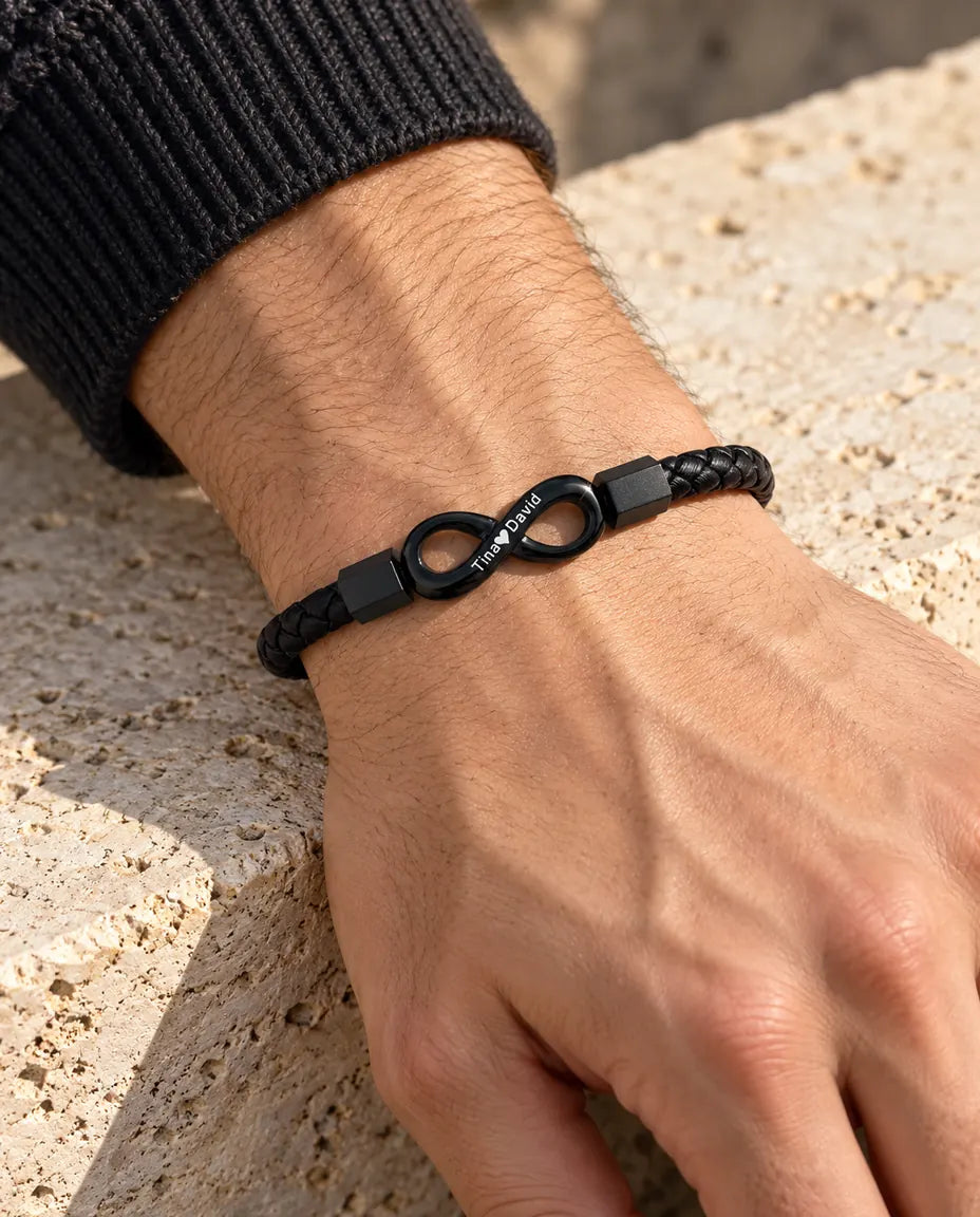 Uomo che indossa al polso il bracciale in similpelle con infinito inciso nero, con un maglione grigio antracite in maglia