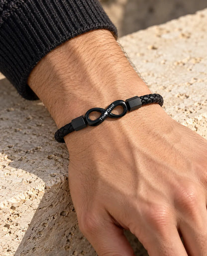 Uomo che indossa al polso il bracciale in similpelle con infinito inciso nero, con un maglione grigio antracite in maglia