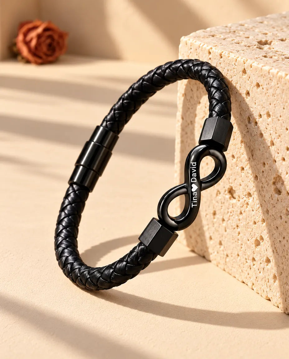 Bracciale in similpelle intrecciata nera con infinito inciso, appoggiato in piedi contro un blocco di travertino