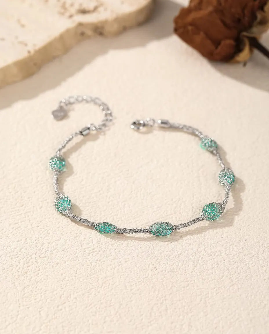 Bracciale Zirconi in Gabbia in Argento 925 - versione con zirconi verdi accanto a una lastra di travertino e a una rosa secca