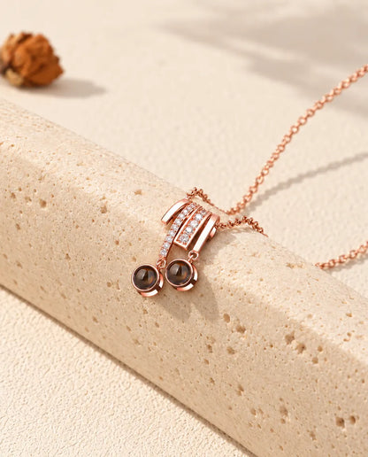 Collana color oro rosa con ciondolo scorrevole e due pietre di proiezione adagiata su un blocco di travertino