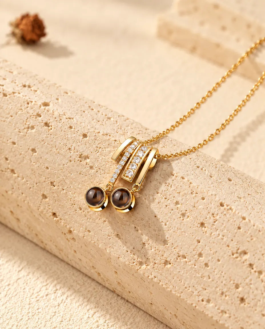Collana dorata con ciondolo scorrevole a pavé e due pietre tonde di proiezione appoggiata sul travertino