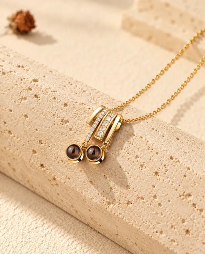 Collana dorata con ciondolo scorrevole a pavé e due pietre tonde di proiezione appoggiata sul travertino