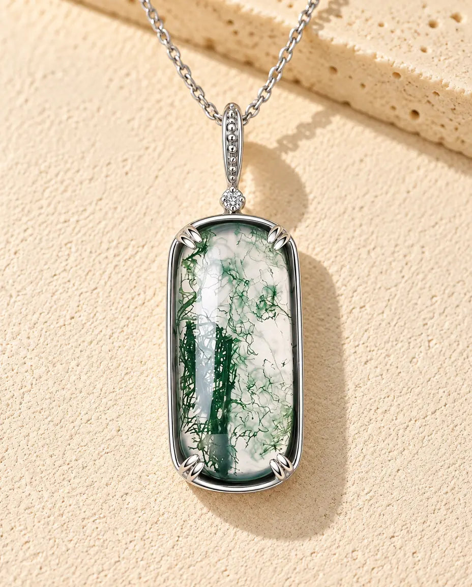 Collana Agata Muschiata Ciondolo Rettangolare in Argento 925 - appoggiata su una superficie chiara ruvida accanto a un blocco di travertino