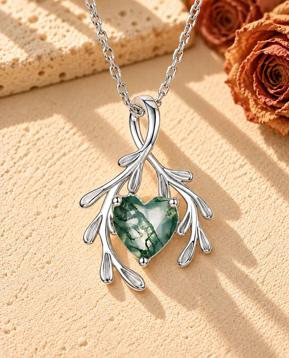 Collana Agata Muschiata Cuore con Rami in Argento 925 - appoggiata su una superficie chiara ruvida accanto a un blocco di travertino