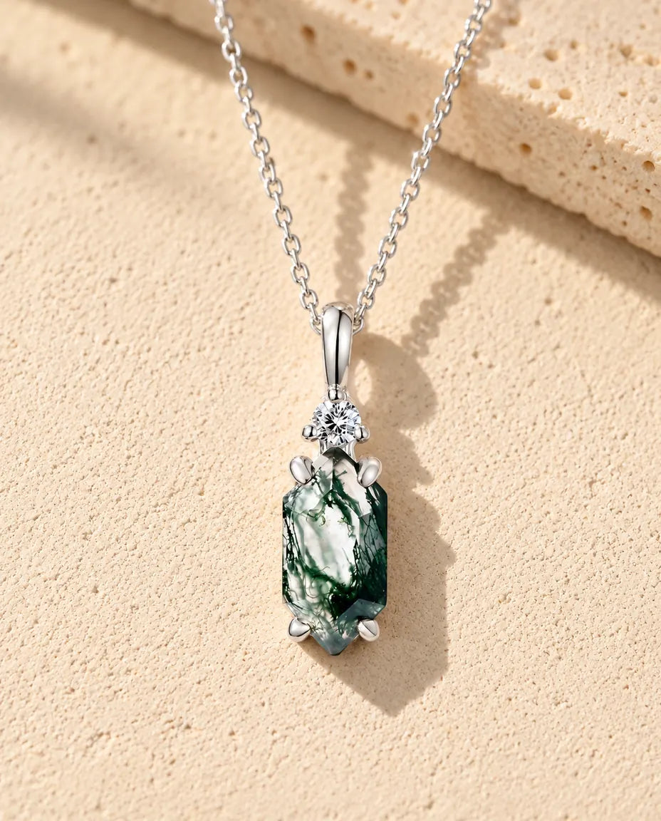 Collana Agata Muschiata Esagono Sottile in Argento 925 - appoggiata su una superficie chiara ruvida accanto a un blocco di travertino