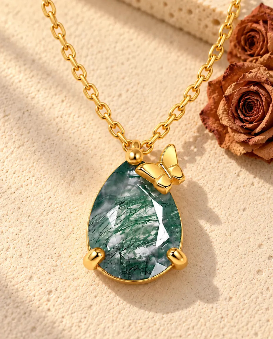 Collana Agata Muschiata a Goccia in Argento 925 Placcato Oro - appoggiata su una superficie chiara ruvida accanto a un blocco di travertino