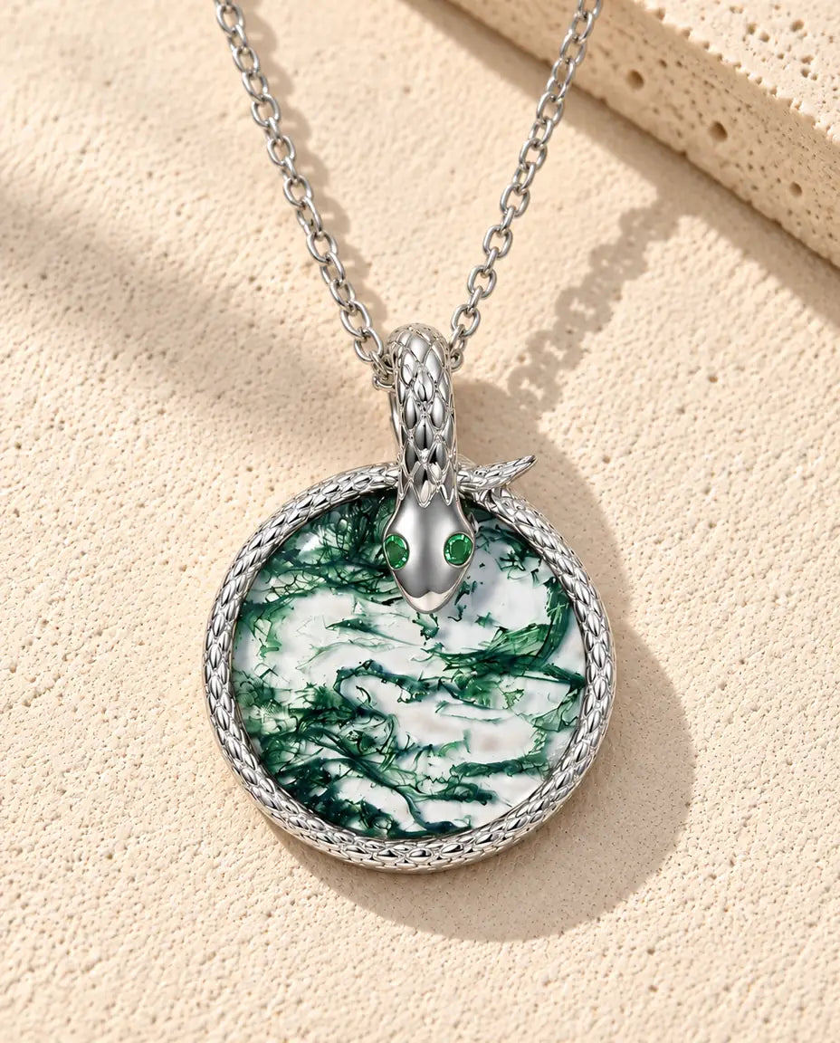 Collana Agata Muschiata Serpente in Argento 925 - appoggiata su una superficie chiara ruvida accanto a un blocco di travertino