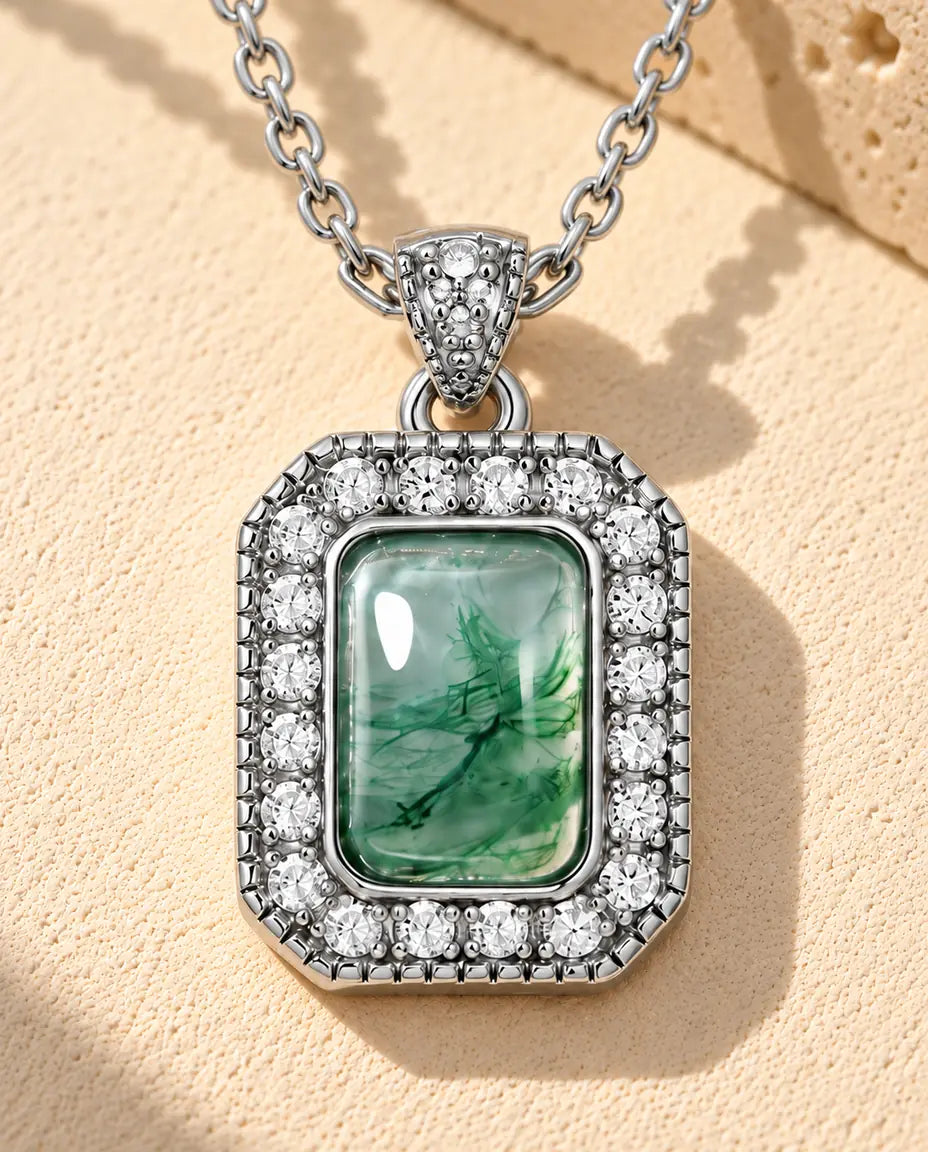 Collana Agata Muschiata Halo in Argento 925 - appoggiata su una superficie chiara ruvida accanto a un blocco di travertino