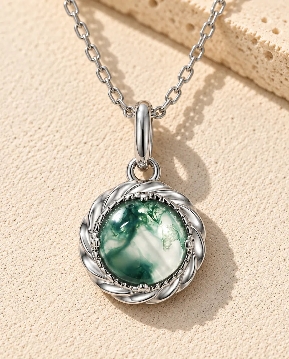 Collana con Ciondolo Agata Muschiata Tondo in Argento 925 - appoggiata su una superficie chiara ruvida accanto a un blocco di travertino
