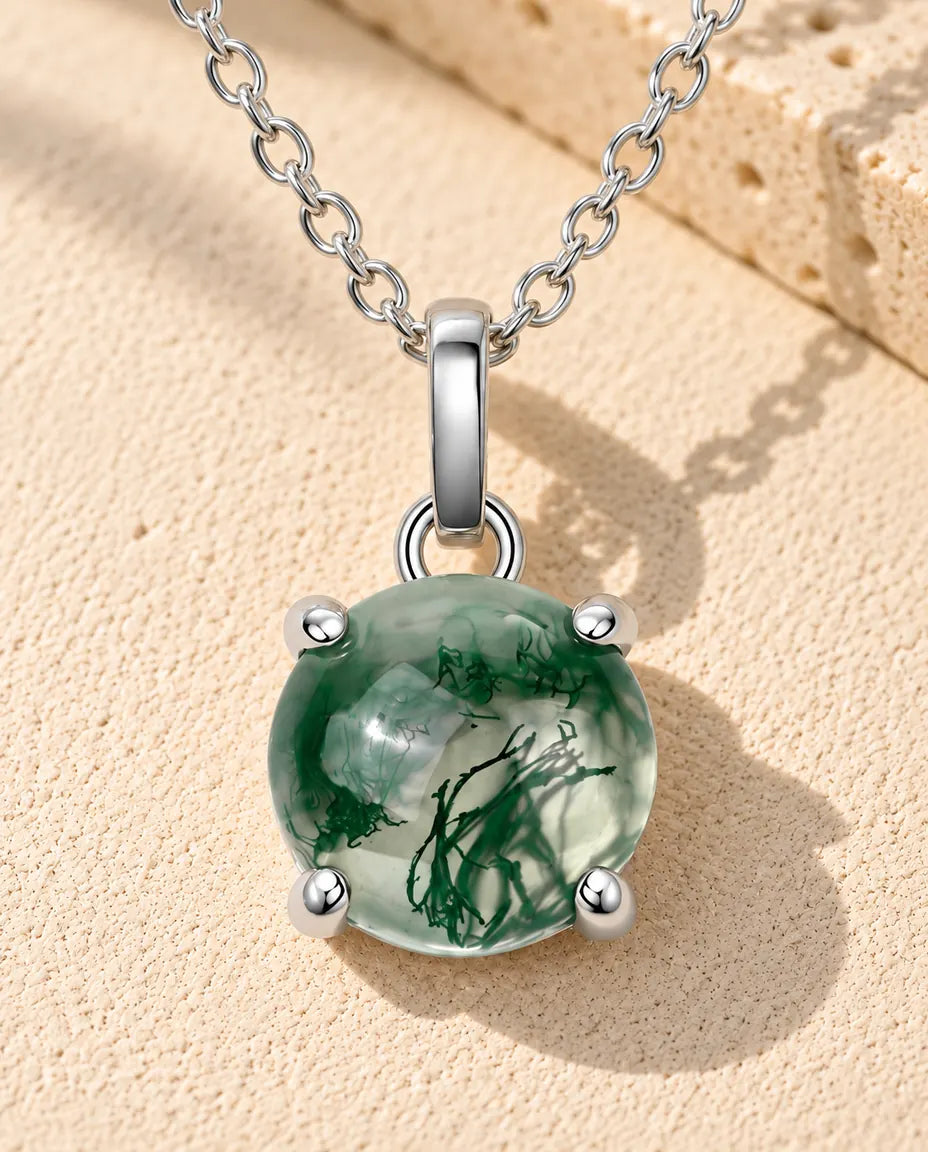 Collana Agata Muschiata Tonda in Argento 925 - appoggiata su una superficie chiara ruvida accanto a un blocco di travertino