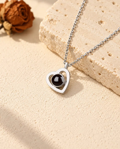 Collana con foto dentro a doppio cuore in argento 925 sul gesso color crema, accanto al travertino