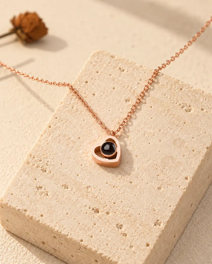 Collana doppio cuore con foto dentro color oro rosa adagiata su un blocco di travertino