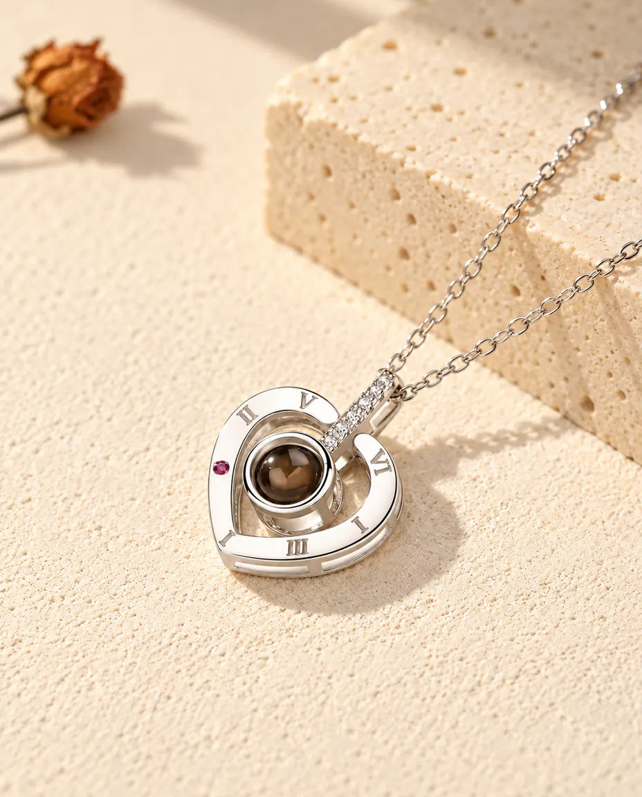 Collana con foto dentro personalizzata in argento 925 con cuore a numeri romani su gesso crema accanto al travertino
