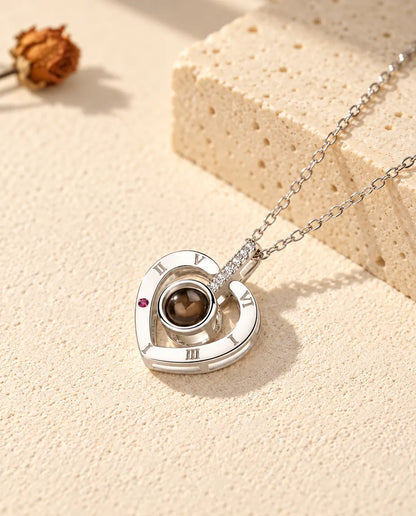 Collana con foto dentro personalizzata in argento 925 con cuore a numeri romani su gesso crema accanto al travertino
