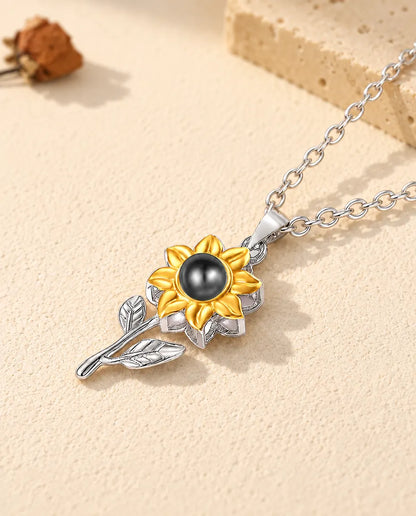 Ciondolo a girasole in argento con due foglie e foto dentro, disteso sul gesso