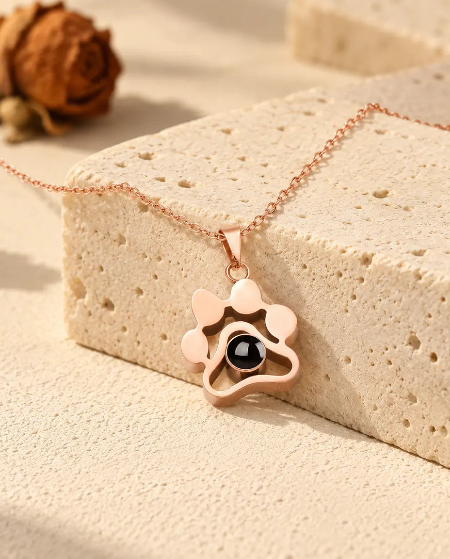 Collana a zampa color oro rosa con foto dentro adagiata sopra un blocco di travertino