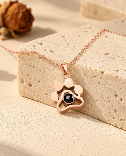 Collana a zampa color oro rosa con foto dentro adagiata sopra un blocco di travertino