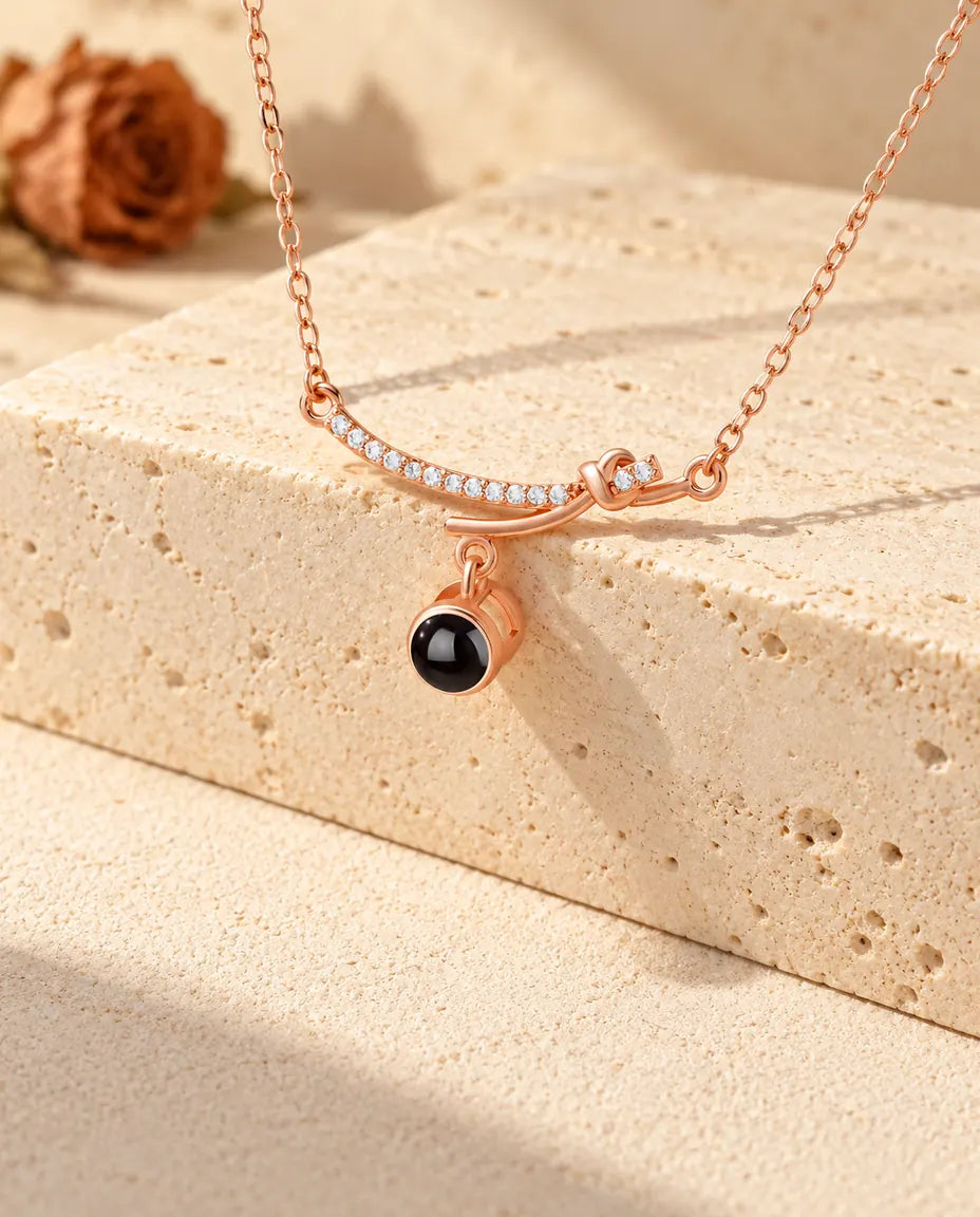 Collana a barra curva color oro rosa con la pietra pendente della foto sopra un blocco di travertino