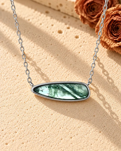 Collana Barretta Agata Muschiata in Argento 925 - appoggiata su una superficie chiara ruvida accanto a un blocco di travertino