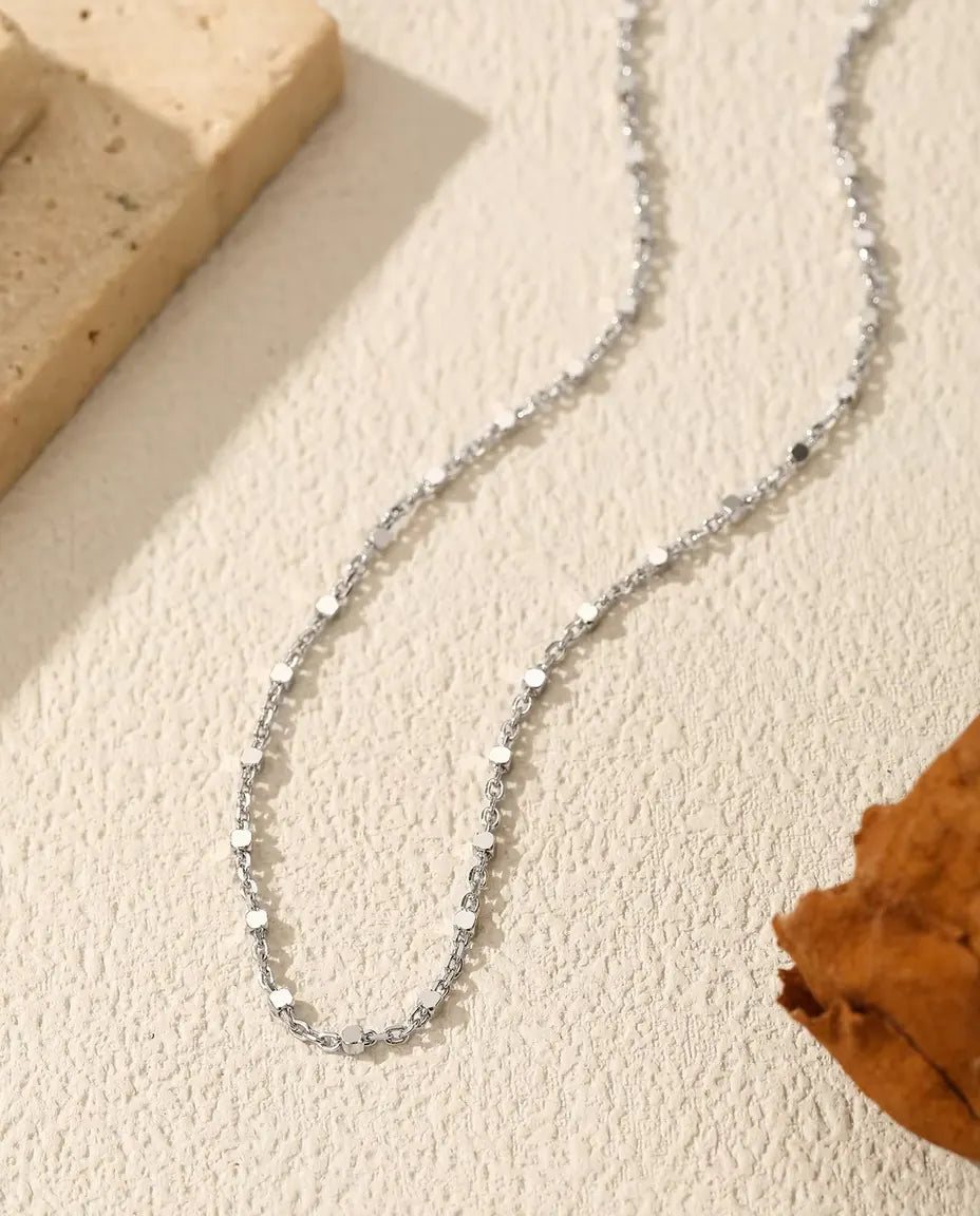 Collana Catena con Paillettes in Argento 925 - adagiata su una superficie chiara accanto a una lastra di travertino