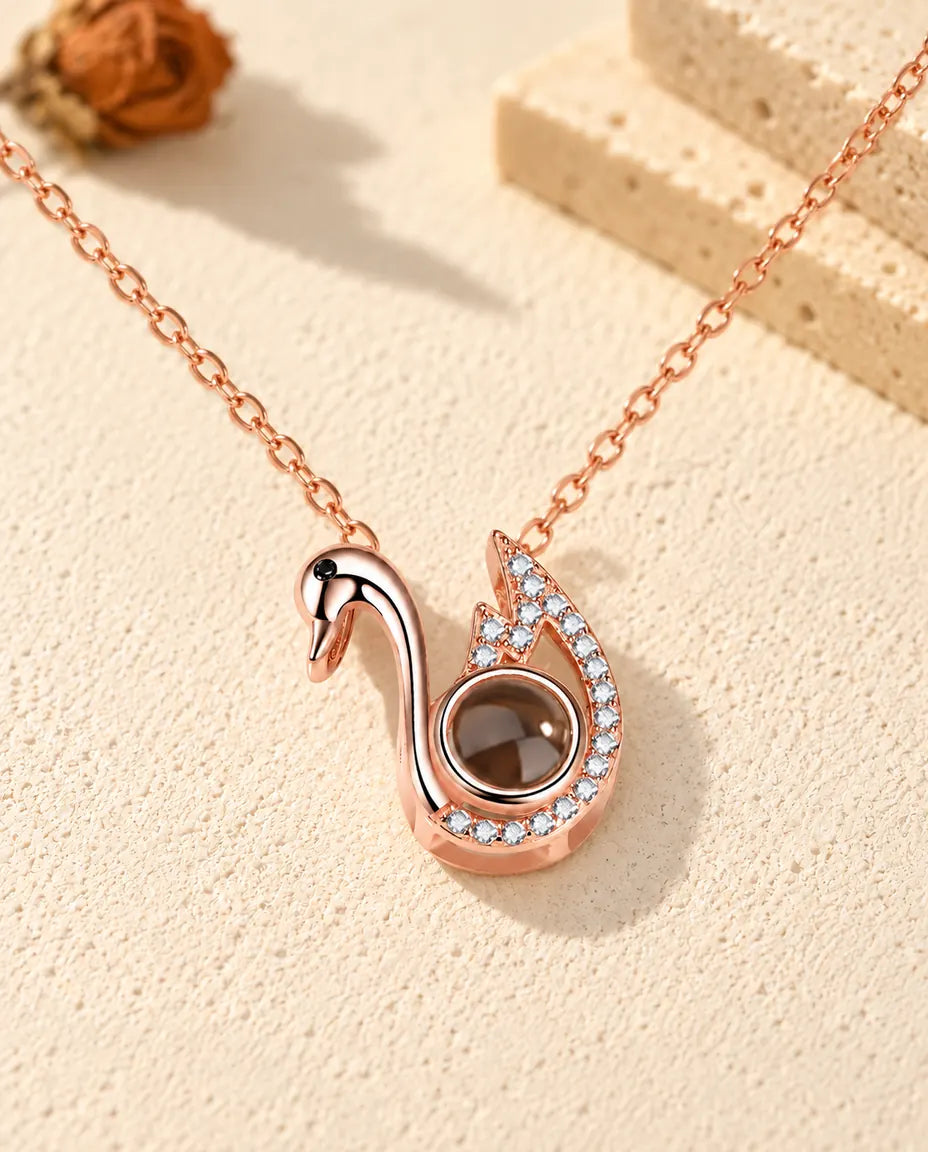 Collana con foto dentro personalizzata a forma di cigno color oro rosa su gesso crema accanto al travertino
