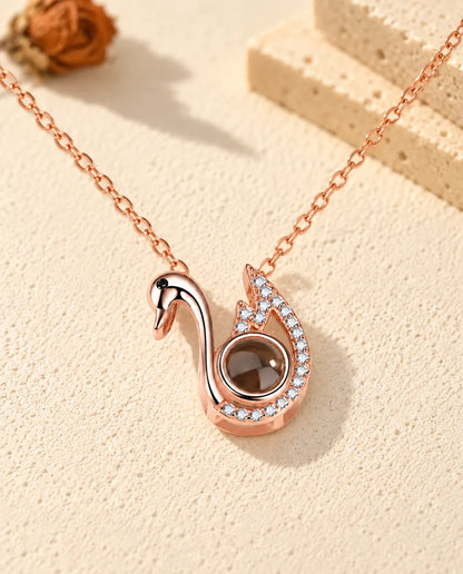 Collana con foto dentro personalizzata a forma di cigno color oro rosa su gesso crema accanto al travertino