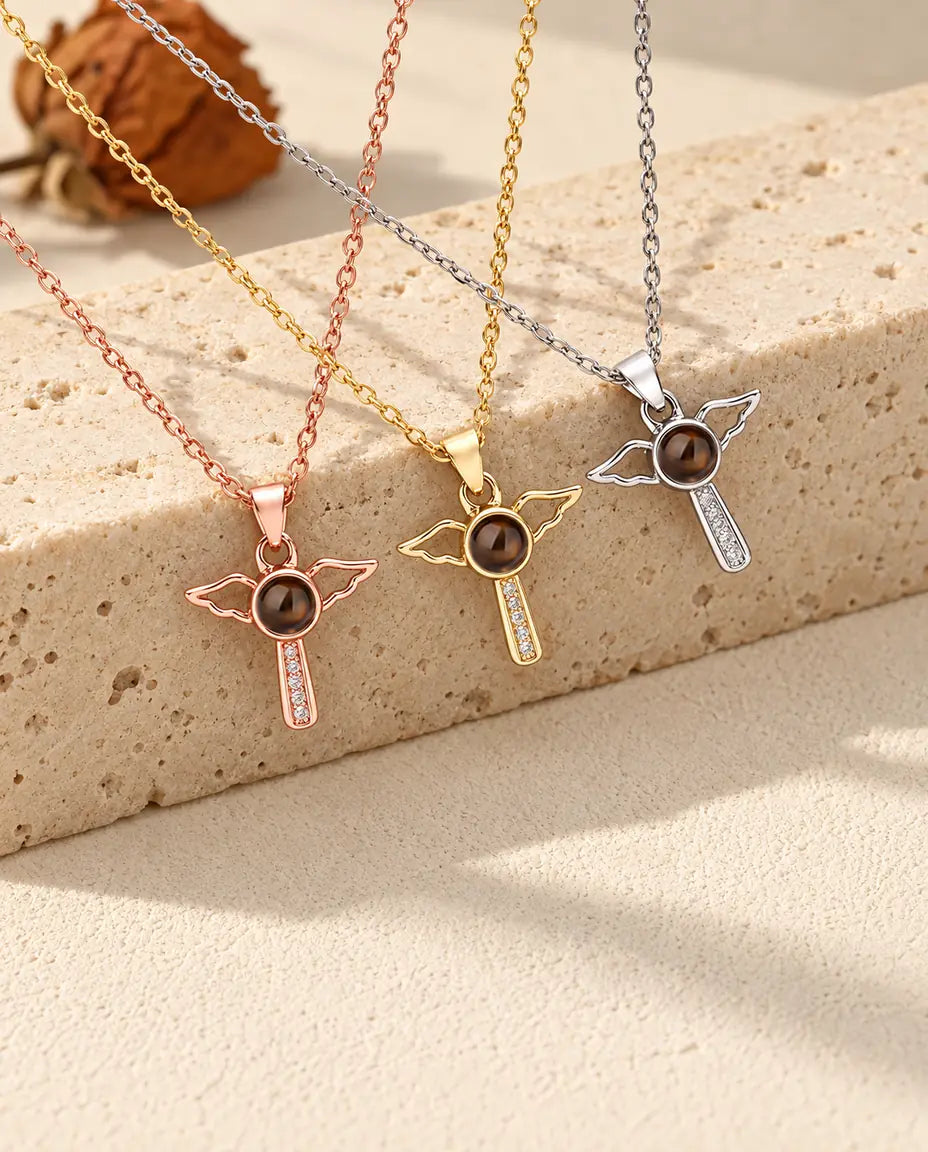 Collane con croce e ali d'angelo in argentato, dorato e color oro rosa adagiate sul travertino