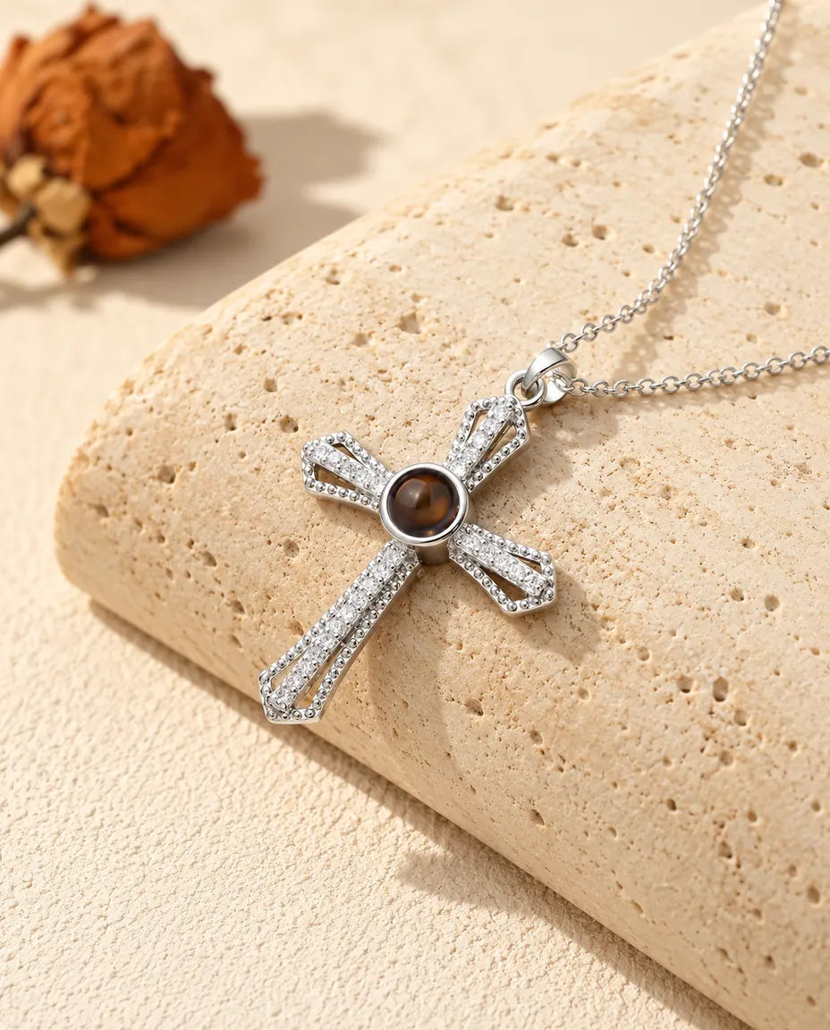 Collana con croce a pavé argentata e foto dentro, con una pietra marrone al centro, su un blocco di travertino