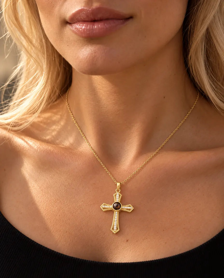 Donna bionda con un top nero che indossa la collana con croce dorata a pavé e foto dentro
