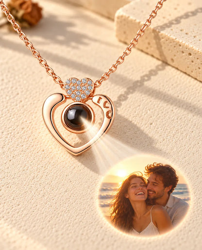 Collana a cuore aperto color oro rosa che proietta sul gesso crema la foto di una coppia al mare