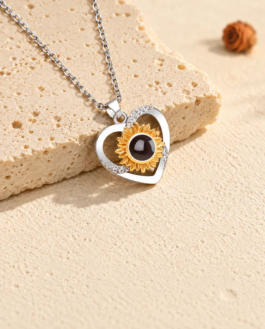 Collana con cuore e girasole e foto dentro, inclinata accanto a una lastra di travertino