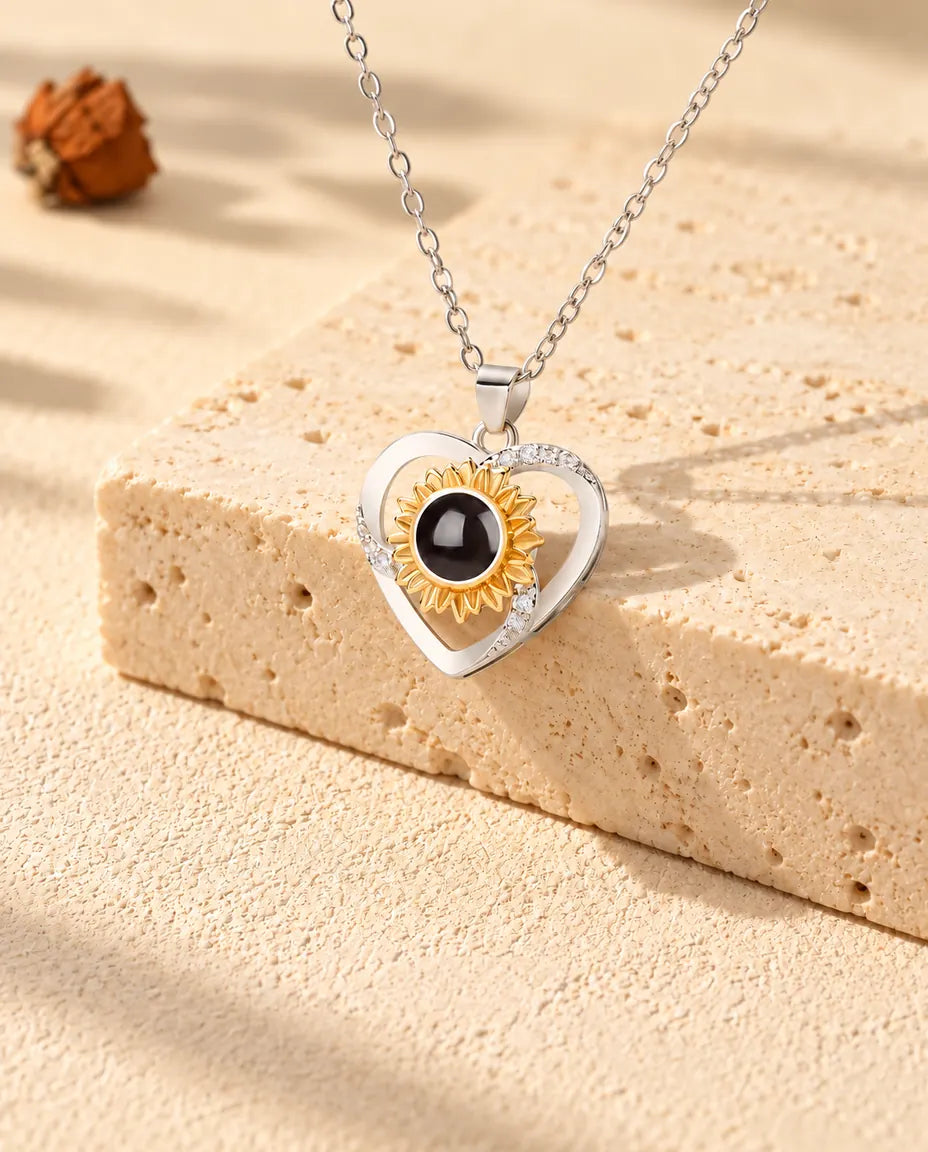 Collana con cuore e girasole e foto dentro adagiata sopra un blocco di travertino