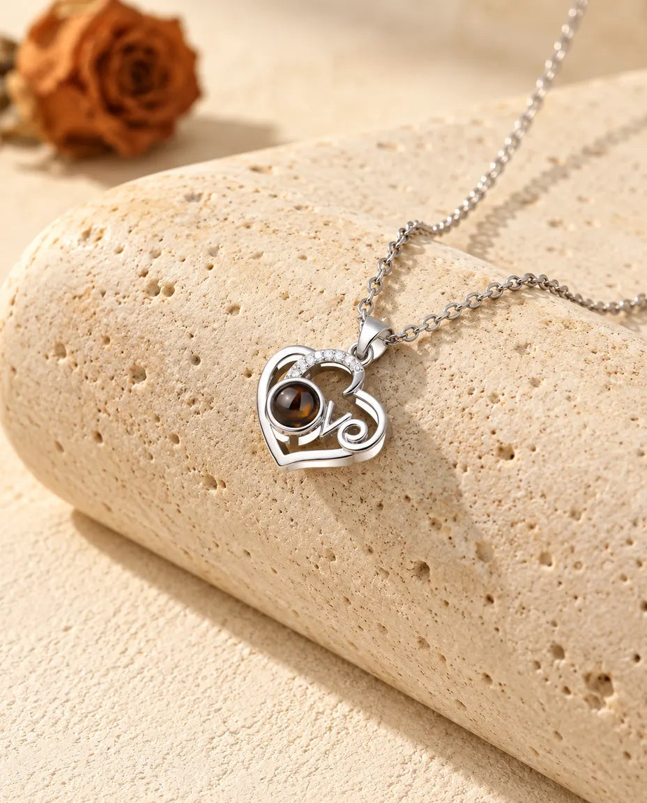 Collana con foto dentro a cuore Love argentata, con arco di zirconi, appoggiata a un blocco di travertino