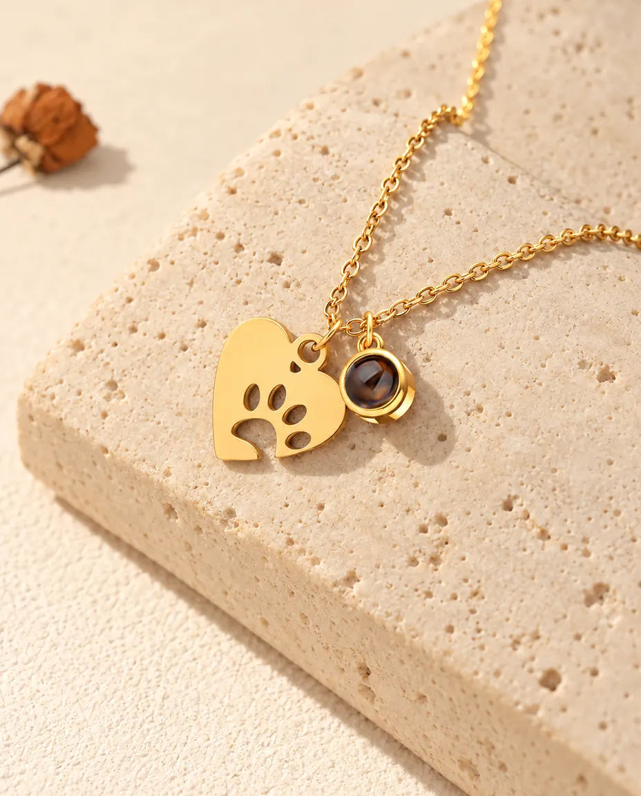 Collana dorata con cuore e zampa e ciondolino con pietra di proiezione su travertino