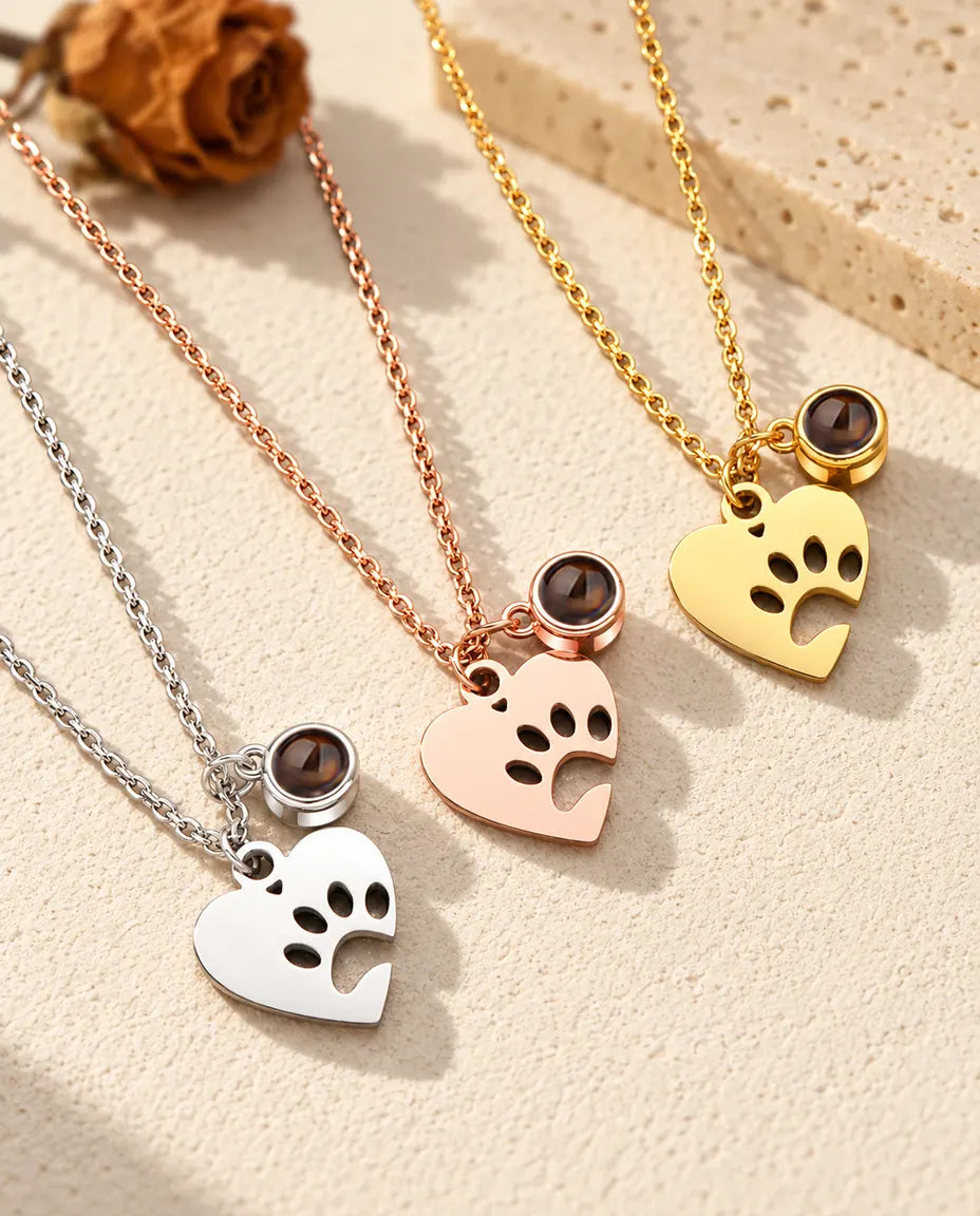 I tre colori della collana con cuore, zampa e foto dell'animale disposti in diagonale su gesso color crema