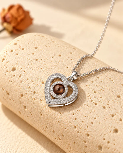 Collana argentata con doppio cuore a pavé di zirconi e foto dentro, su un blocco di travertino
