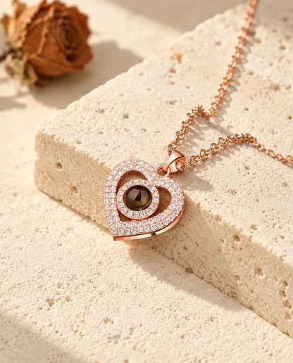 Ciondolo a doppio cuore color oro rosa a pavé appoggiato a un blocco di travertino