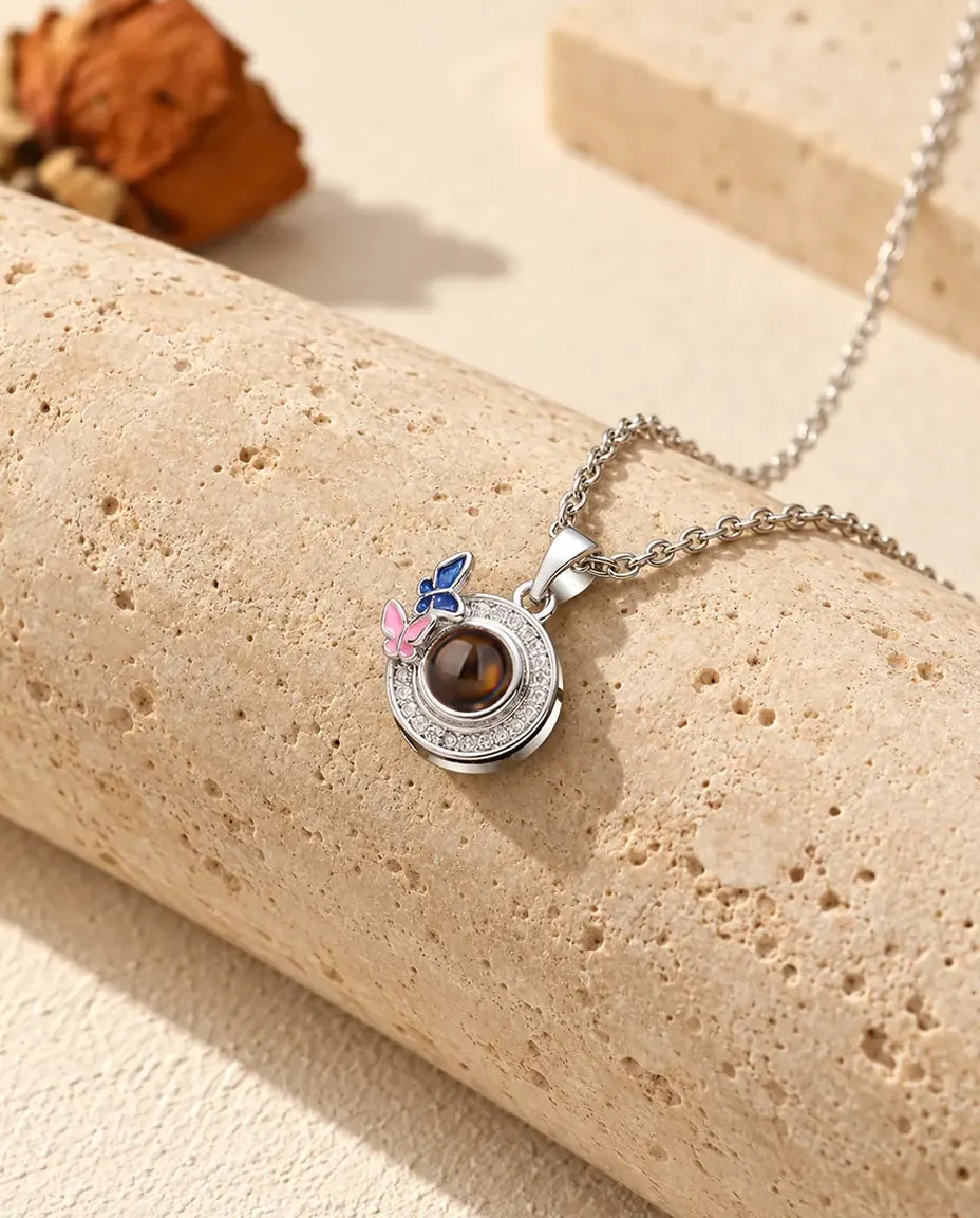 Collana argentata con foto dentro, ciondolo tondo e farfalle smaltate blu notte e rosa, su travertino