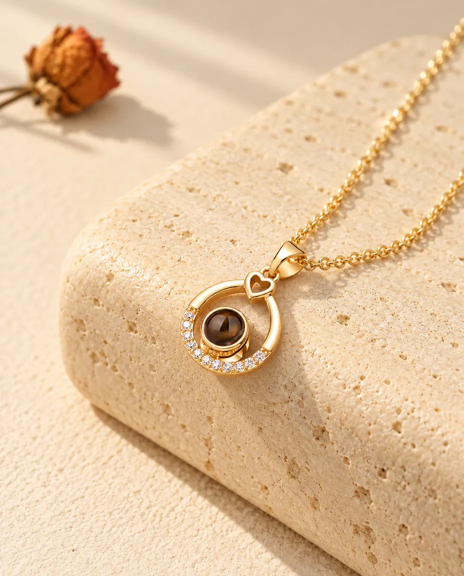 Collana personalizzata dorata a goccia con un piccolo cuore in cima e foto dentro, sul travertino