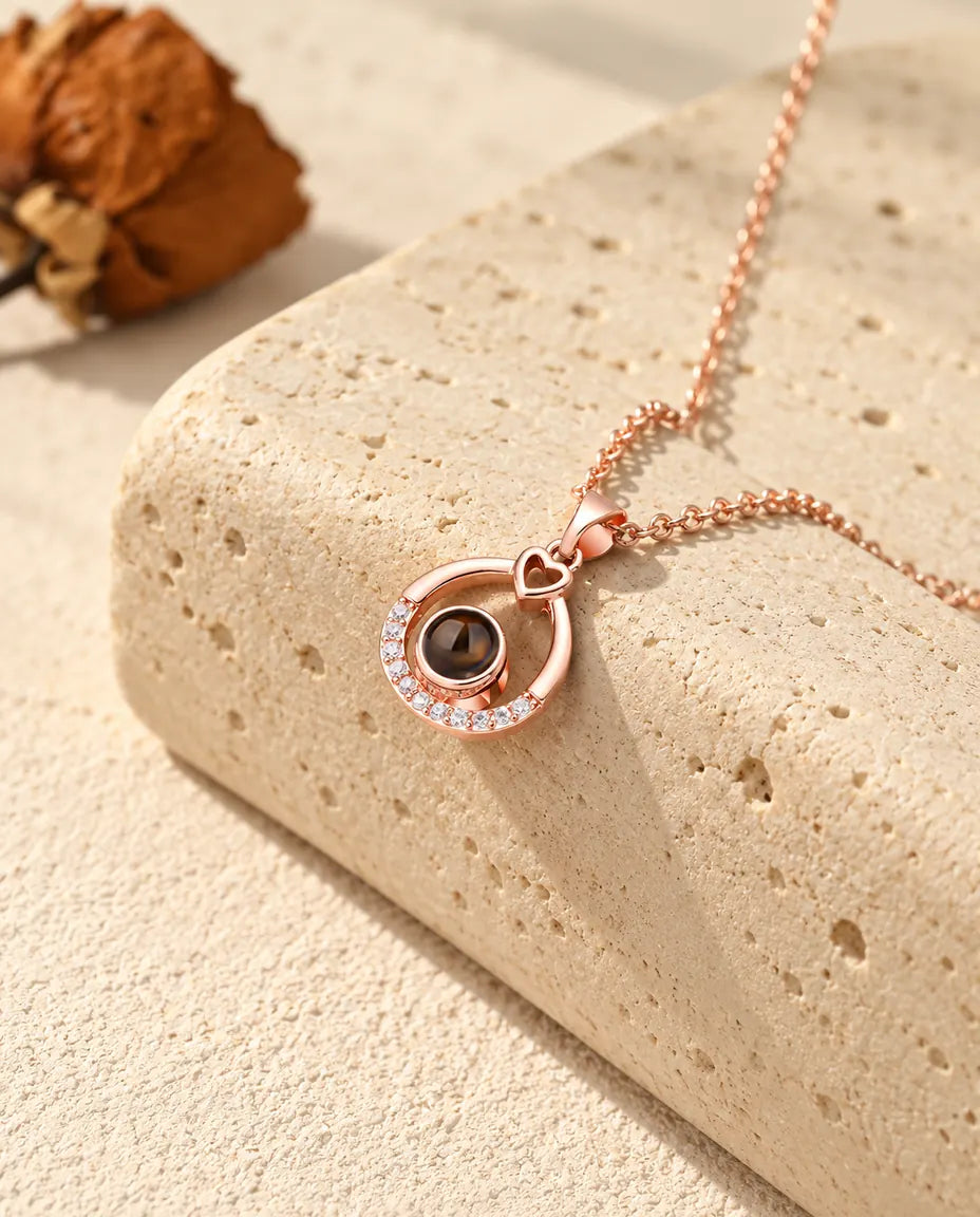 Collana color oro rosa a goccia con foto dentro appesa davanti a un blocco di travertino