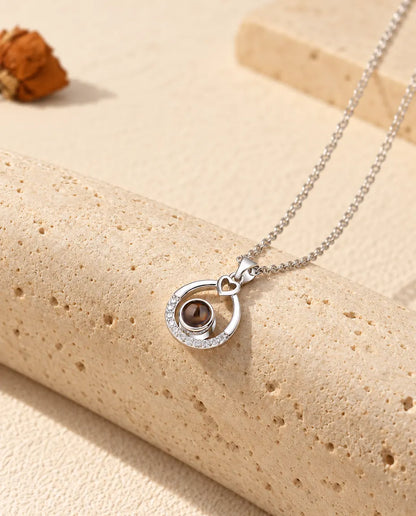 Collana argentata a goccia con foto dentro appesa davanti a un blocco di travertino