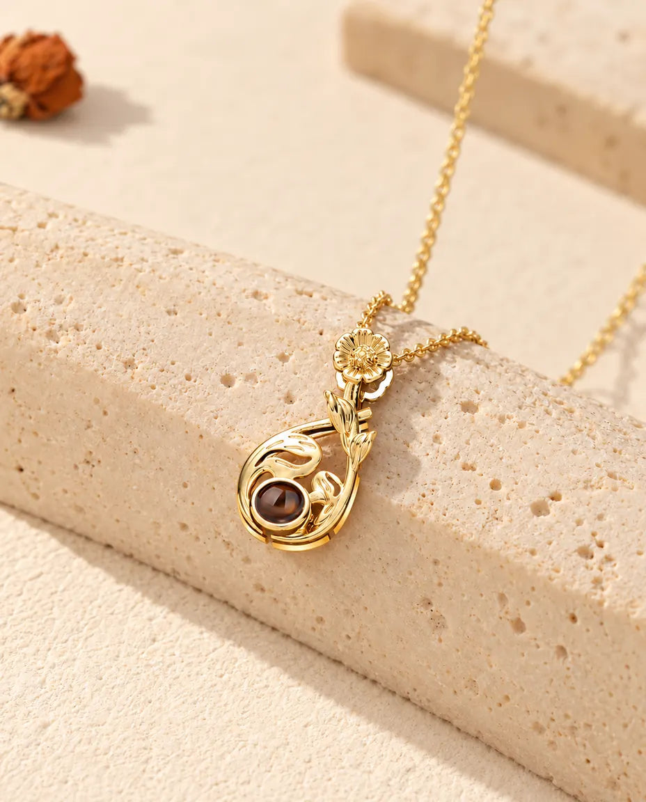 Collana personalizzata dorata a goccia di foglie con margherita e foto dentro, sul travertino