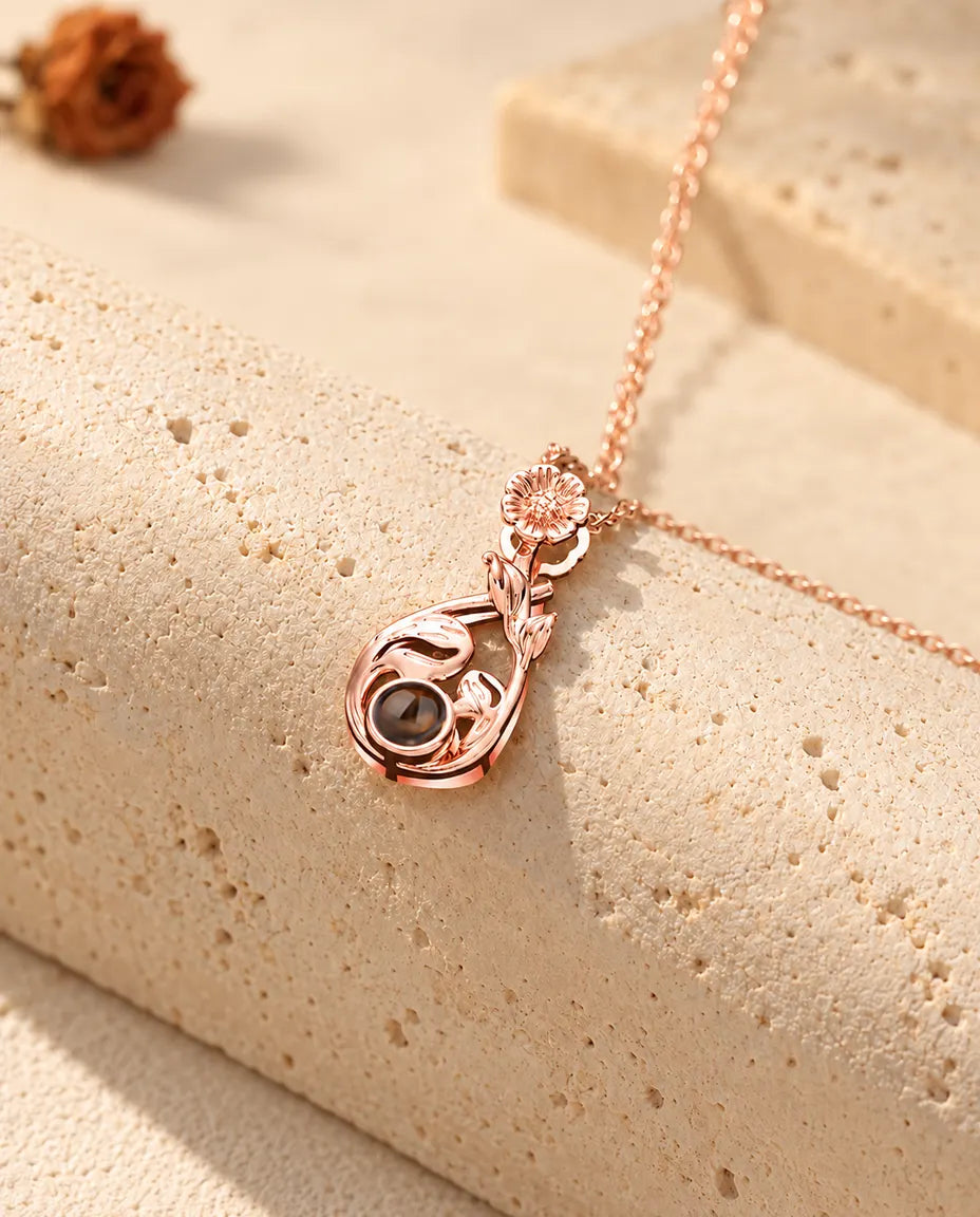 Collana color oro rosa a goccia con margherita appesa davanti a un blocco di travertino