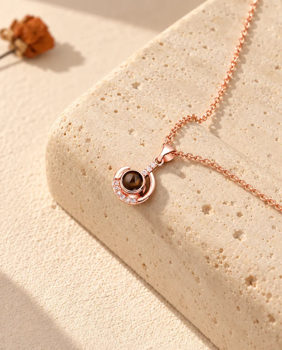 Collana personalizzata color oro rosa a mezzaluna con foto dentro, su un blocco di travertino