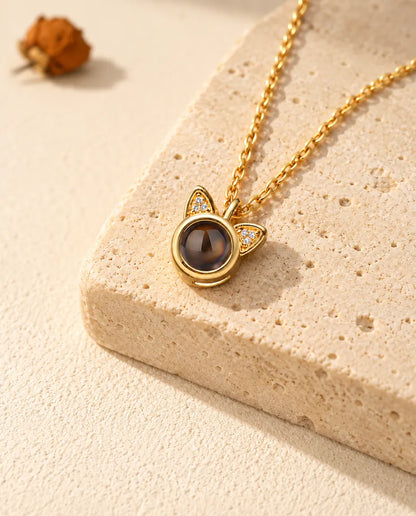 Collana personalizzata dorata con orecchie di gatto e foto dentro, appoggiata su un blocco di travertino
